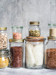 Glass jars with various noodles cereals and seeds on a grey background