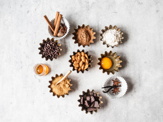 Baking ingredients: flour, brown sugar, egg, cocoa, almond, dark chocolate and spices on grey background. Top view.