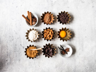 Baking ingredients: flour, brown sugar, egg, cocoa, almond, dark chocolate and spices on a grey background. Top view.
