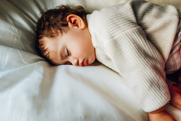 Obraz premium Baby sleeps peacefully during a nap at noon lying on a fluffy white cushion.