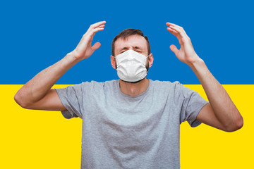 man with a medical mask on his face raised his hands up in panic and despair on the background of the Ukrainian flag 