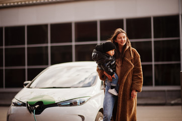 Young mother with child charging electro car at the electric gas station.