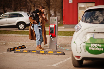 Young mother with child charging electro car at the electric gas station.