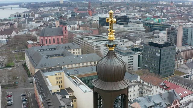 Aerial / drone close rotating cinematic shot of the cross on top of the christus church in mainz with the river rhine with ships and the Mainzer dom in the background 25p