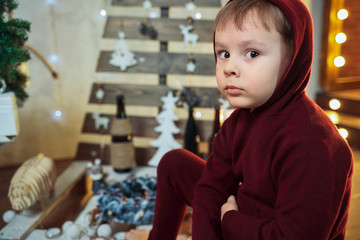 A boy in a hoodie squints at the camera directly and waits for a gift for Christmas. Portrait of a child in a new year's atmosphere with space for copying.