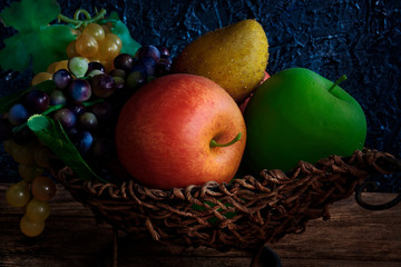 Artificial fruits lie in a wicker basket. Still life with dark lighting. Background.