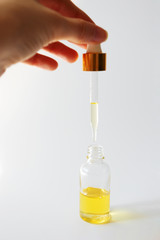 Serum in glass bottle and human hand holding pipette on light background. Skincare beauty product, vertical