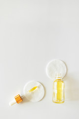 Vitamin E in glass bottle and pipette on cotton pads on white background, copy space. Skincare beauty product, above