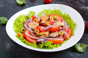 Salad of marinated mussels, fresh tomatoes, red onions, olives in a bowl on a black background