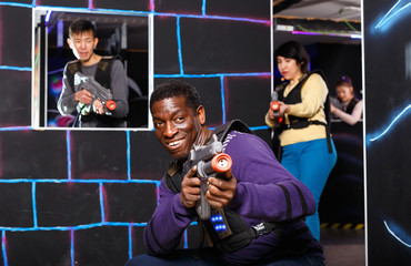 Portrait of cheerful African-American with laser gun having fun on dark laser tag arena