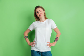 Smiling, confident. Caucasian young woman's portrait on green studio background. Beautiful female model in white shirt. Concept of human emotions, facial expression, sales, ad, youth.
