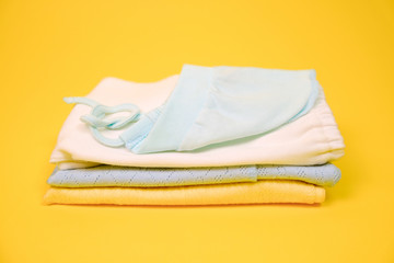 Heap of baby clothes on vibrant yellow background.