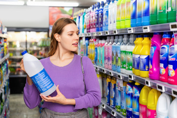 Young woman buying household chemicals or laundry detergent at supermarket