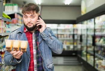 man choosing milk yogurt in supermarket and talking by phone