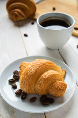 two croissants and a cup of coffee on a white wooden table