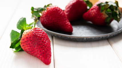 strawberry berries on a wooden board in a metal bowl on a white table close-up
