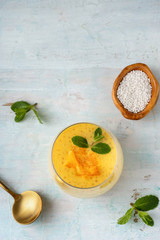 Vertical shot of a glasss with orange tapioca pudding on aqua mint background