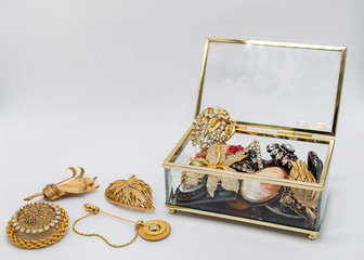  Open transparent glass box, inside which and next to it are gold and silver vintage jewelry with...
