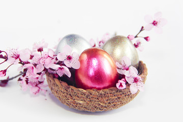Easter multicolored shiny eggs and natural pink sakura flowers in a decorative basket