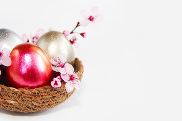 Easter multicolored shiny eggs and natural pink sakura flowers in a decorative basket