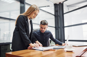 Woman and man in formal clothes working together indoors in the office by table