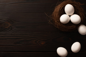 top view of white chicken eggs in nest and on brown wooden background