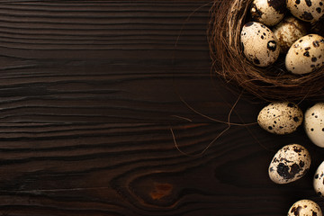 top view of quail eggs in brown nest on and on dark wooden surface