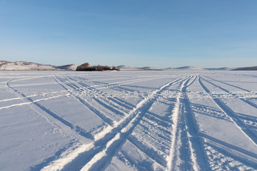 Beautiful geometric patterns from the wheels of cars were imprinted on the snowy plain of the lake against the shore.