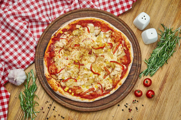 Hawaiian pizza with melted cheese, pineapples, chicken, corn on a wooden tray. Pizza in composition with ingredients on a wooden table. Top view.