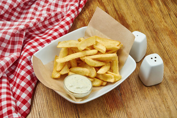 French fries in craft paper on a gray plate on a wooden background. American traditional fast food. Street food