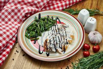 Baked chicken fillet with cream sauce and asparagus side dishes in a ceramic plate on wooden background. Close up