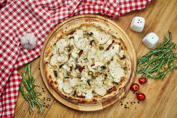 Pizza with smoked chicken, mushrooms, olives, tomatoes, cheese and white sauce on a wooden tray. Pizza in composition with ingredients on a wooden table