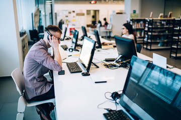 Attentive male student in headphones using computer while doing homework in library