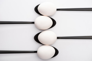 top view of white chicken eggs on black spoons on white background