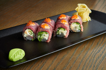 Fresh tuna rolls, dorado, caviar, cucumber and Philadelphia cheese on a black plate on a wooden background. Japanese sushi roll