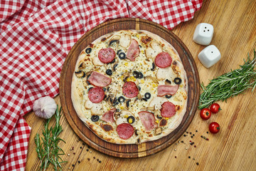 Pizza with with smoked chicken, ham, salami, olives and white sauce on a wooden tray. Pizza in composition with ingredients on a wooden table
