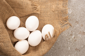top view of white chicken eggs on sackcloth on grey concrete background