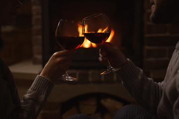 Couple with glasses of red wine near burning fireplace, closeup