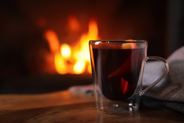 Tasty mulled wine, plaid and blurred fireplace on background