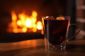 Tasty mulled wine, plaid and blurred fireplace on background