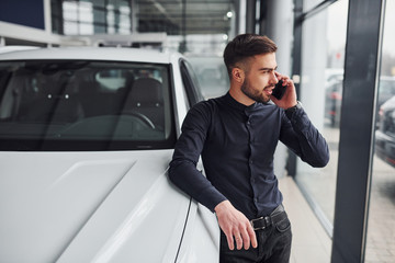 Young man in formal clothes is near brand new expensive car