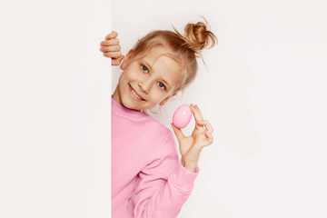 A girl on an Easter egg hunt. The girl holds the egg in her hand and looks out from behind the door. Children celebrate the spring holiday. Happy Easter, the concept of the Easter holiday