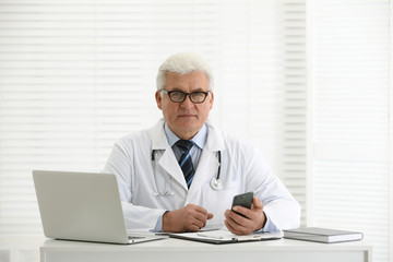 Fototapeta na wymiar Senior doctor with smartphone at table in office