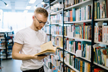 Adult student reading book while standing in library