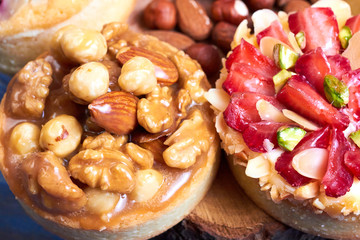 Mini tarts cupcakes with strawberries, walnuts, almond, nuts and blueberries on blue wooden background. Close up