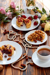 Cup of coffee and three cut mini tarts cupcakes with strawberries, blueberries and with walnuts, almonds and hazelnuts on plate