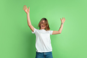 Dancing, hair flying. Caucasian young woman's portrait isolated on green studio background. Beautiful female model in white shirt. Concept of human emotions, facial expression, sales, ad, youth.