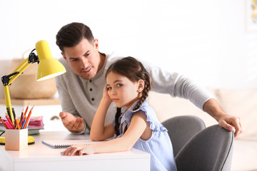 Father scolding his daughter while helping with homework at table indoors - obrazy, fototapety, plakaty