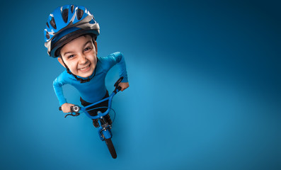 funny little boy with a bicycle in a helmet on a blue background. top view. studio photo