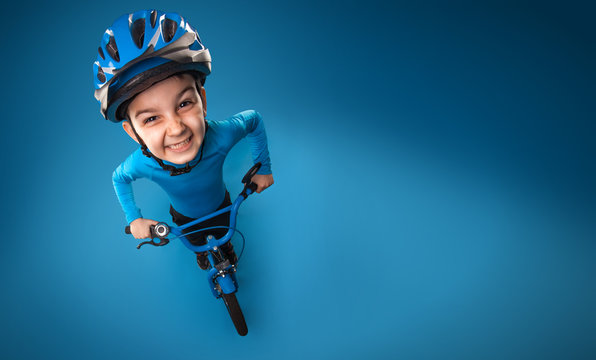funny little boy with a bicycle in a helmet on a blue background. top view. studio photo